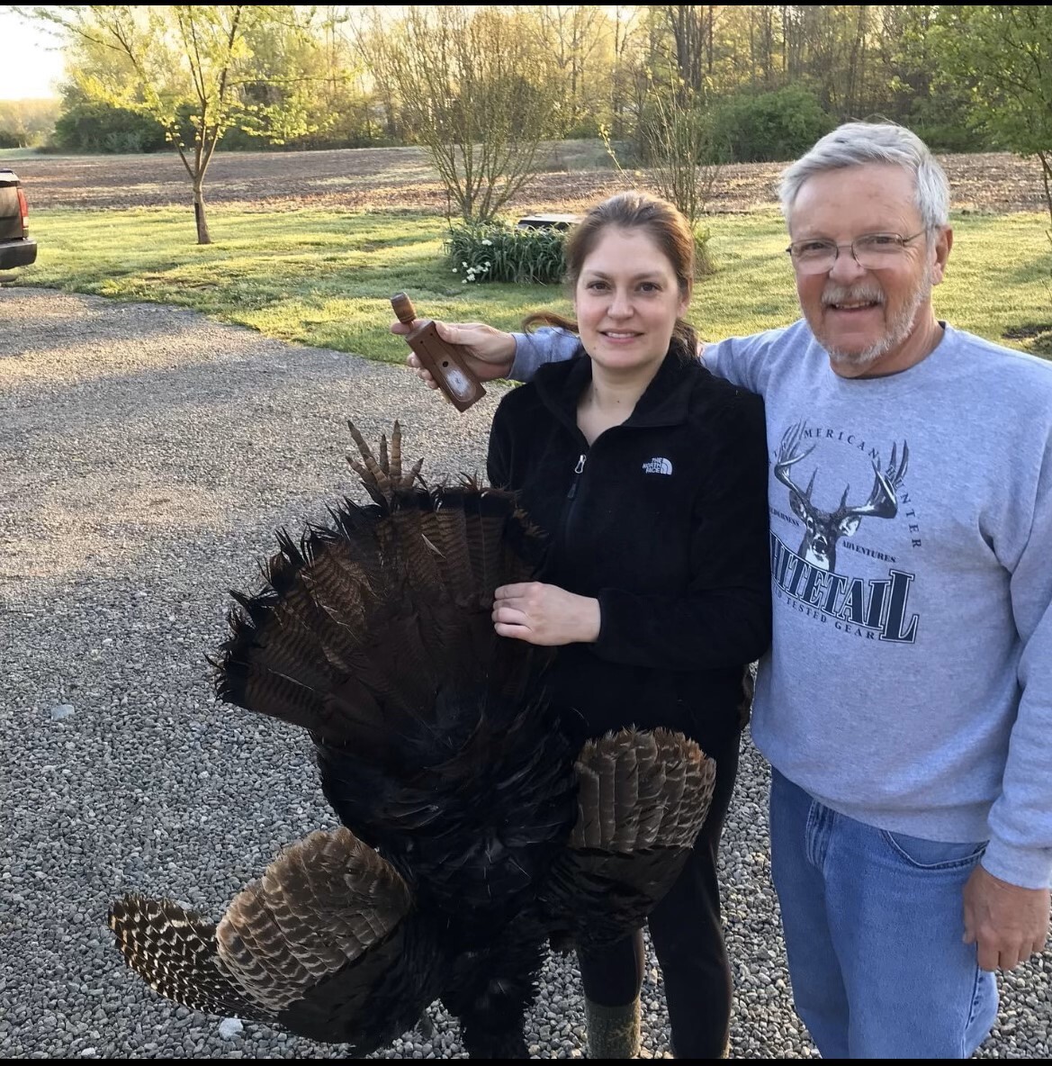 Two people holding a turkey in front of a field